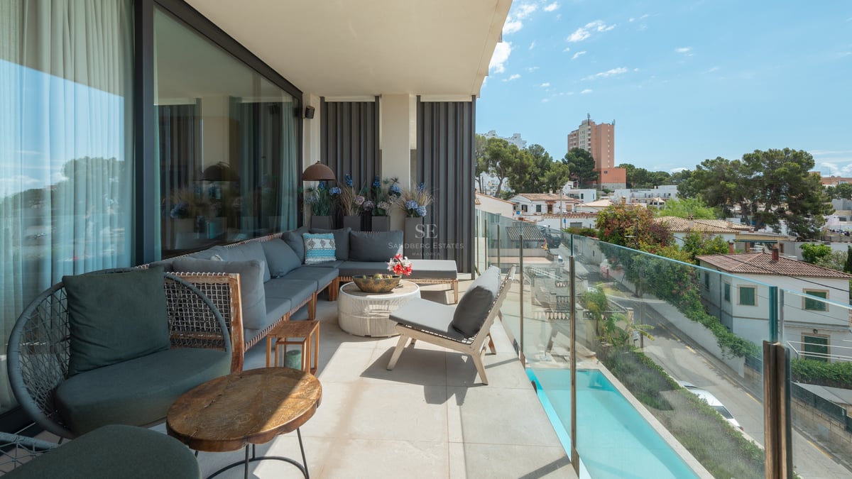 Vaste balcon moderne avec mobilier gris, garde-corps en verre et vue sur le quartier et la piscine au soleil.