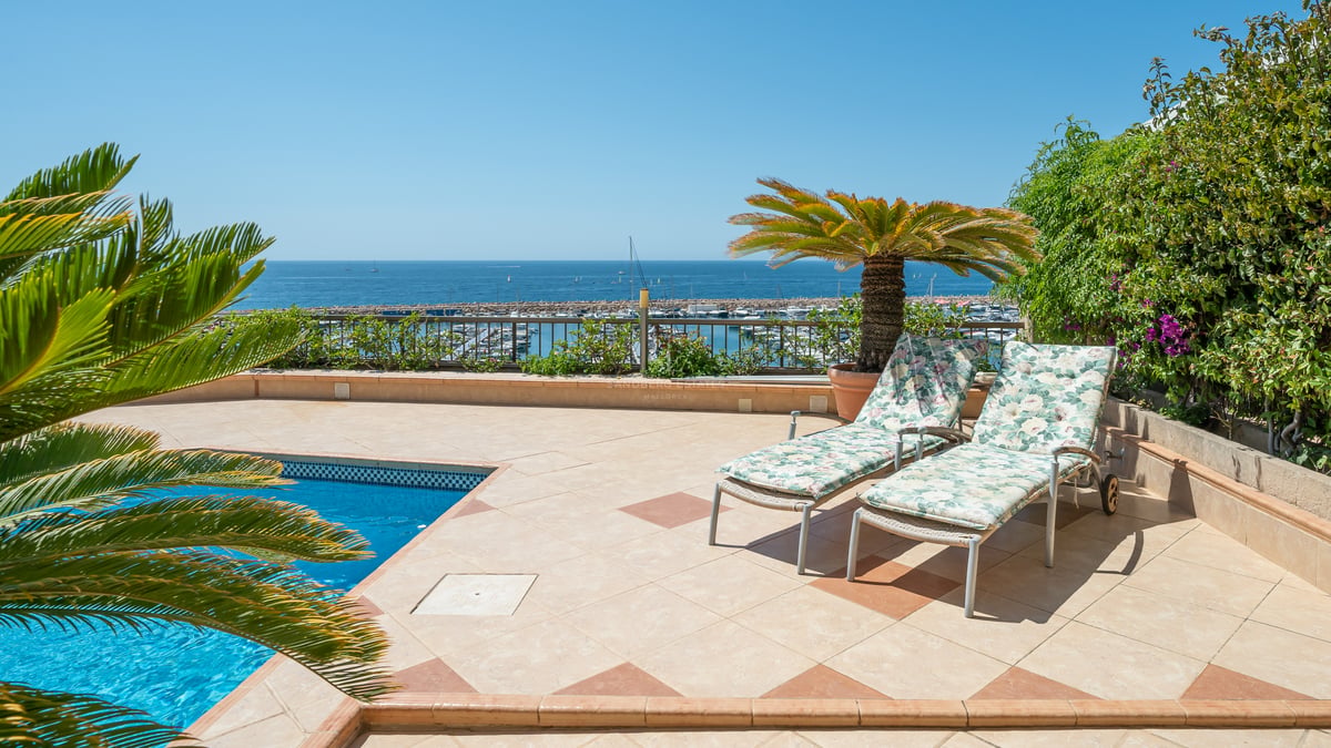 Terrasse surélevée avec piscine, chaises longues et vue panoramique sur un port de plaisance et la mer Méditerranée.