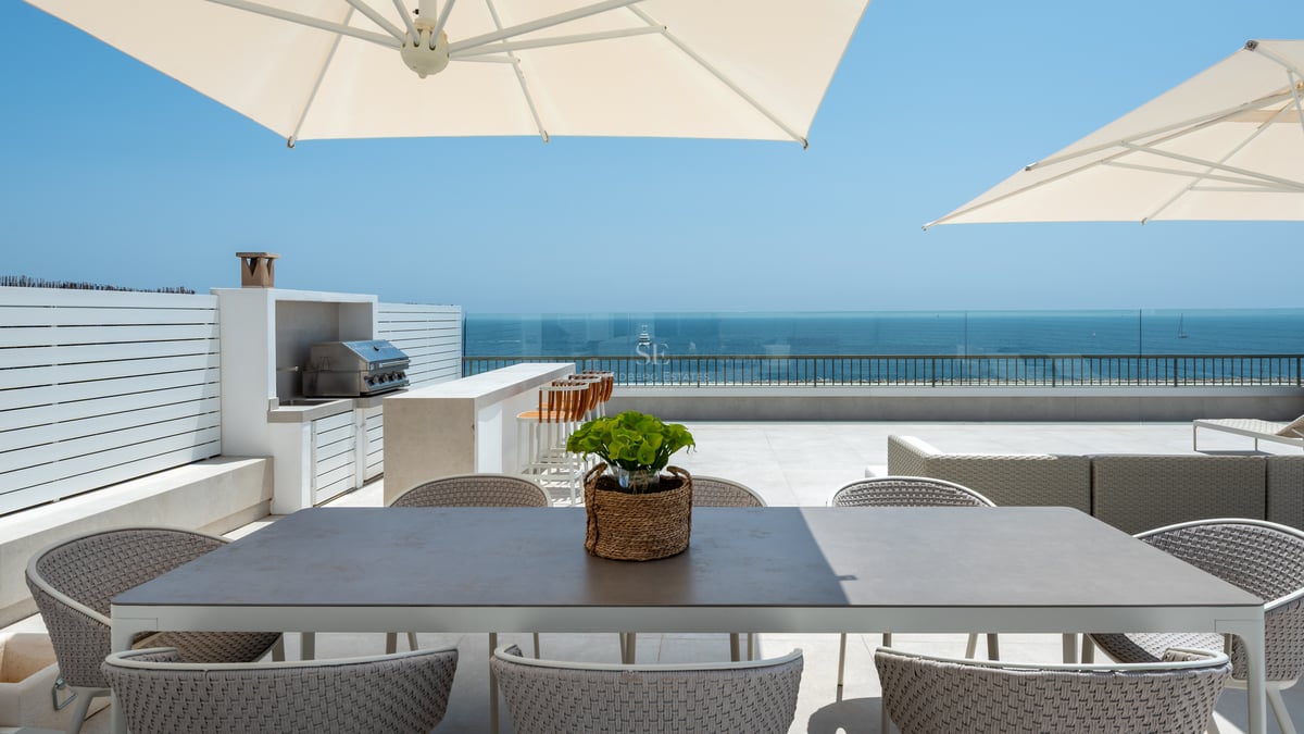 Toit-terrasse de luxe avec coin repas, cuisine d'été et garde-corps en verre surplombant la mer Méditerranée.
