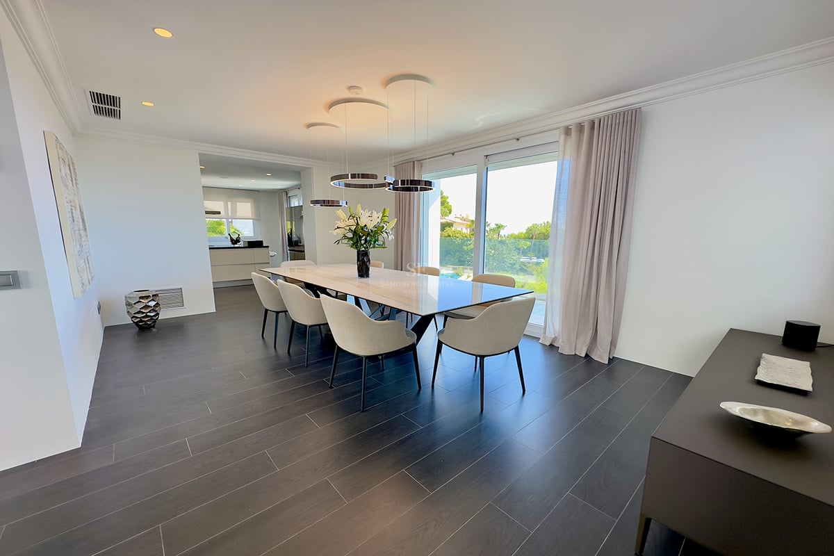 Salle à manger minimaliste avec table en marbre, chaises beiges, parquet foncé et grandes fenêtres sur le jardin.