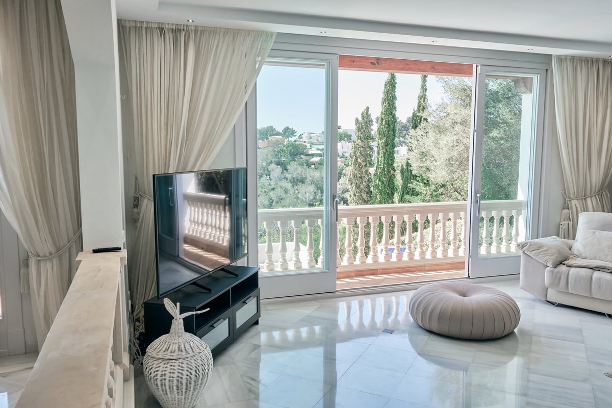 Salon avec sol en marbre poli, grandes baies vitrées ouvrant sur une terrasse avec balustrade en pierre et vue verdoyante.