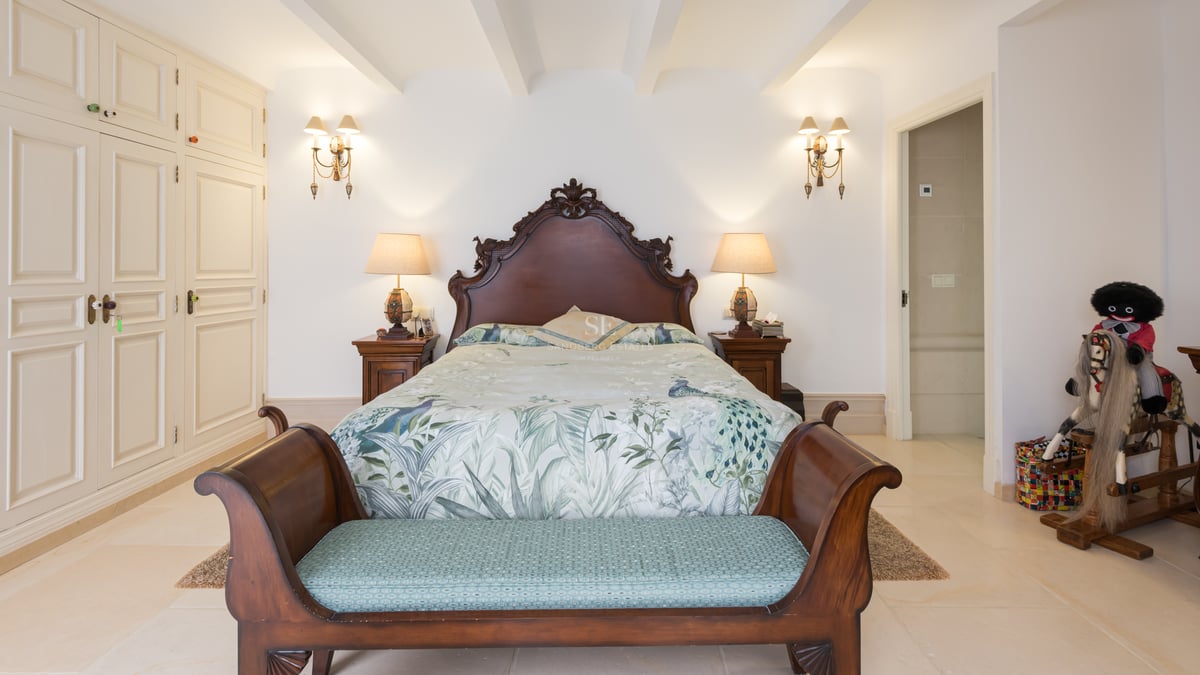 Chambre avec lit en bois sculpté, literie florale, banc au pied du lit et armoires encastrées blanches.