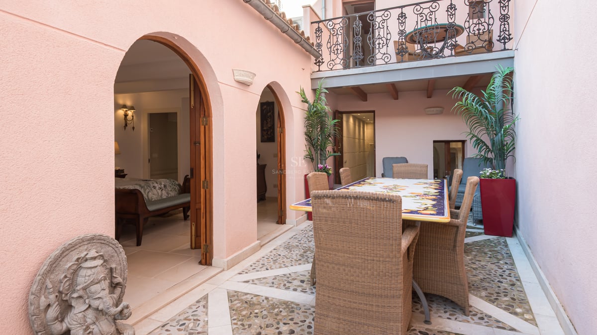 Patio privé avec sol en mosaïque de galets, mobilier en osier et murs roses aux arcades élégantes.