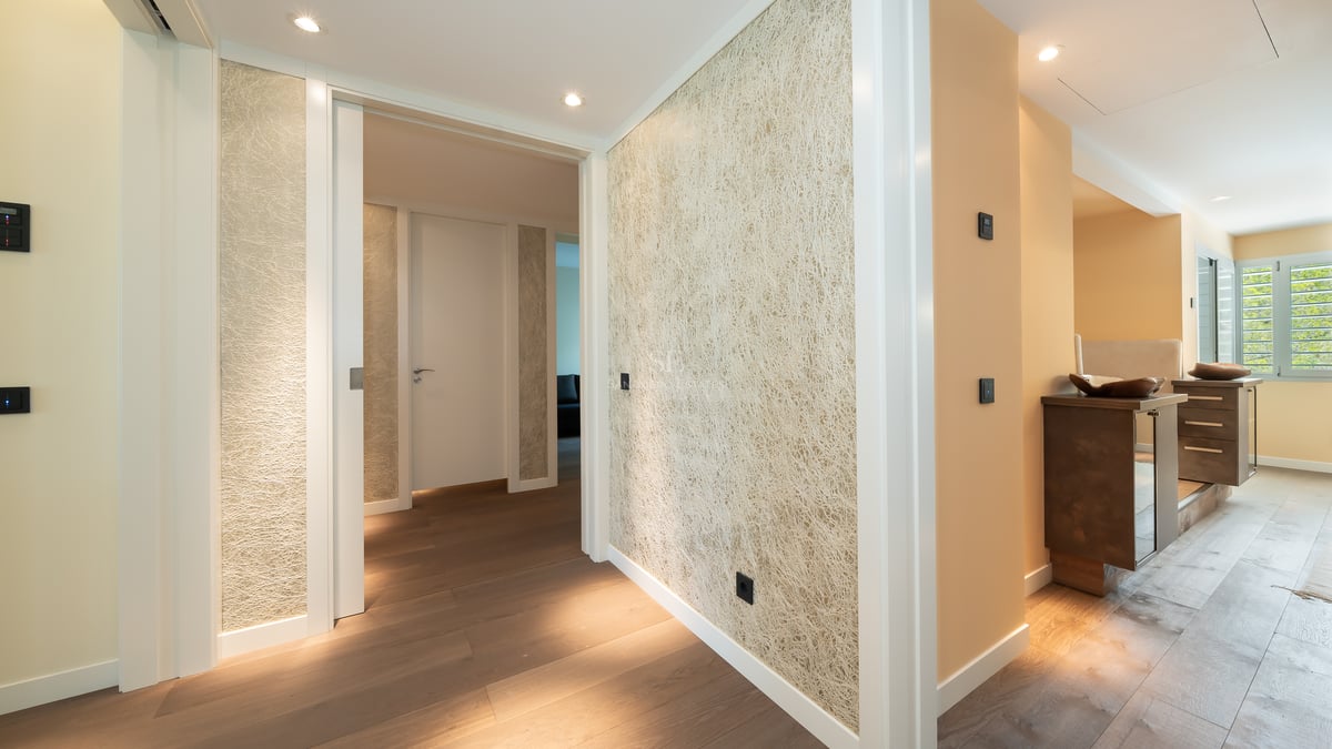 Couloir de luxe avec parquet en chêne, papier peint texturé et éclairage encastré menant aux pièces privées.