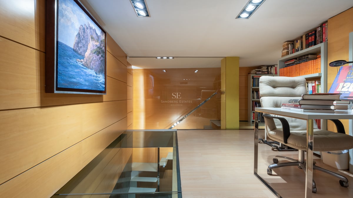 Modern home office featuring a glass floor staircase, light wood wall paneling, and built-in bookshelves.