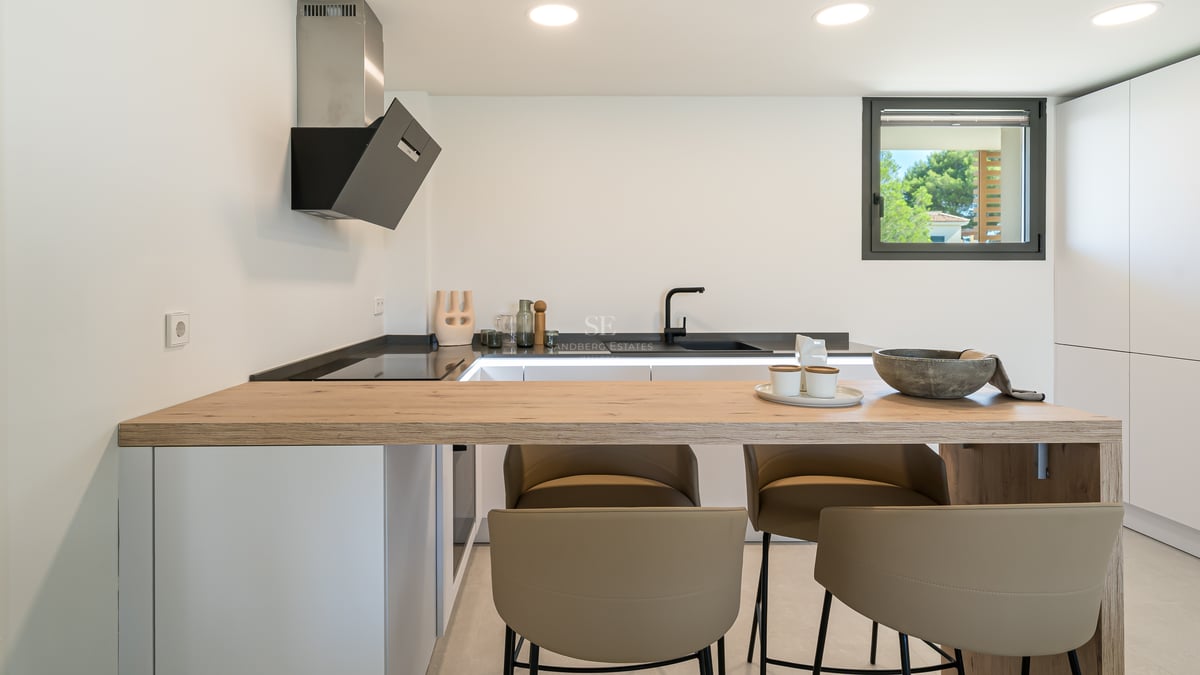 Cocina contemporánea blanca con barra de desayuno de roble natural, grifería negra y taburetes de diseño.
