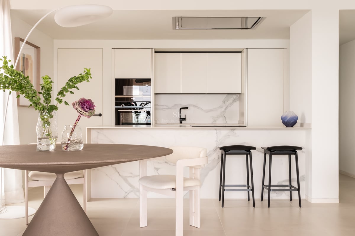 Cuisine minimaliste avec îlot en marbre Calacatta, appareils intégrés et coin repas avec table ronde.