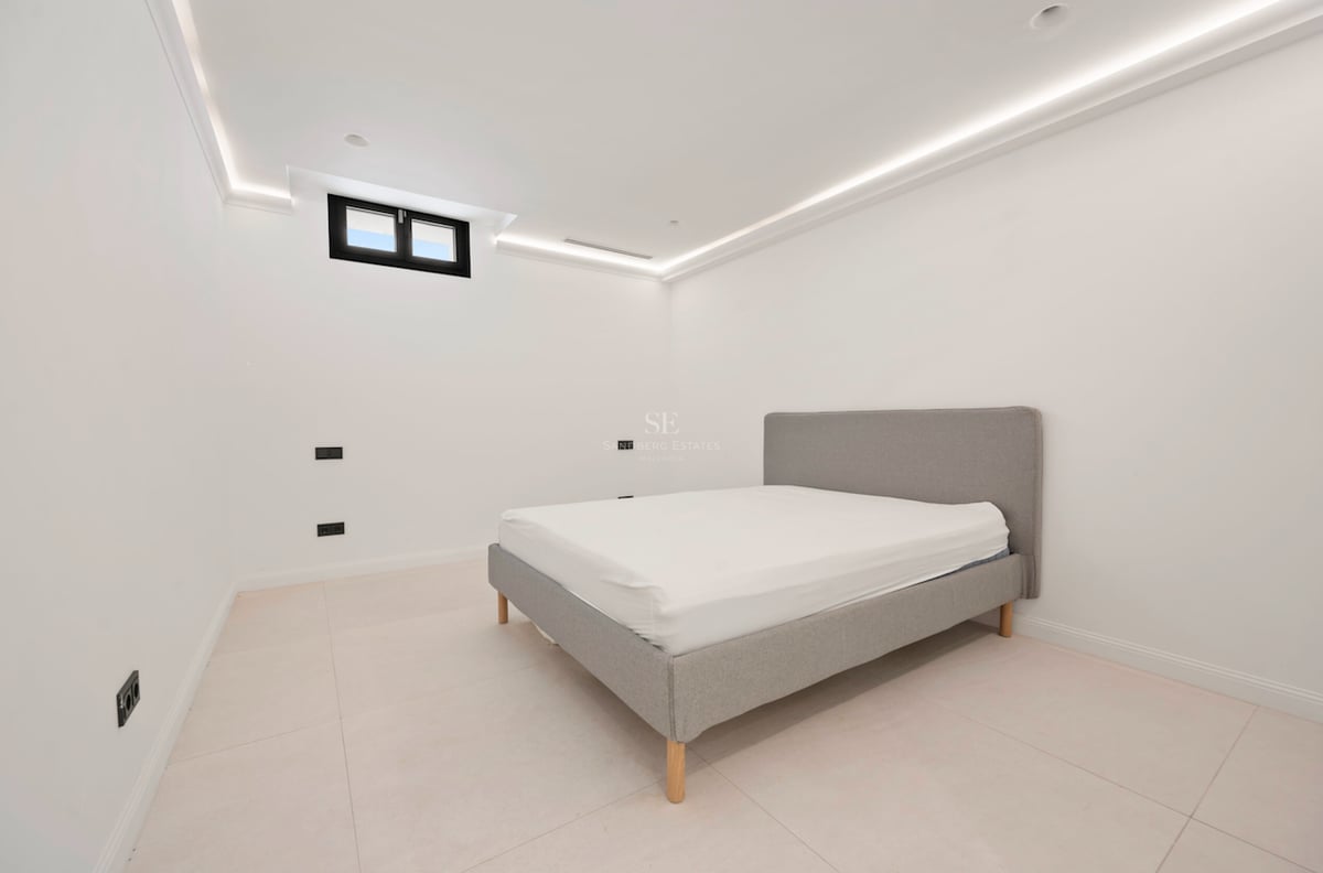 Chambre moderne avec lit tapissé gris, sol en grès cérame clair et corniche lumineuse LED au plafond.