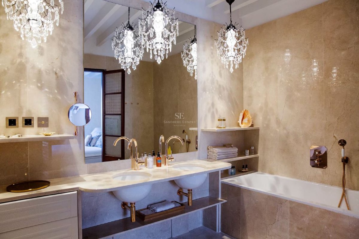 Cuarto de baño de lujo con dos lavabos, grifos de oro, paredes de mármol y tres lámparas de araña de cristal.