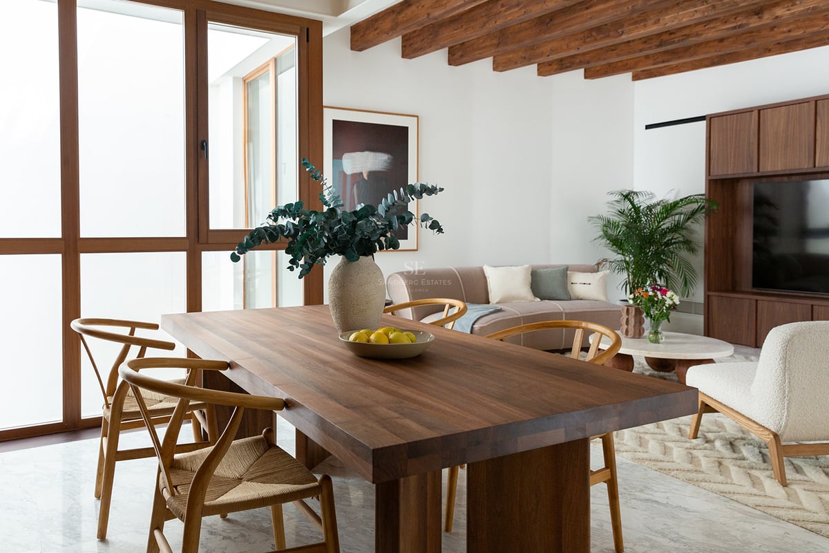 Comedor moderno con mesa de nogal, sillas de estilo Wishbone, vigas de madera vistas y suelos de mármol.