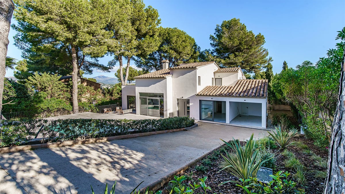 Une villa blanche moderne de deux étages avec des tuiles en terre cuite, entourée de grands pins et d'un espace piscine.