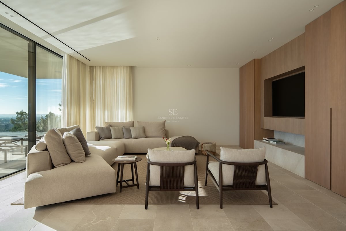 Salon moderne avec canapé d'angle beige, mur TV boisé et grandes baies vitrées offrant une vue panoramique.