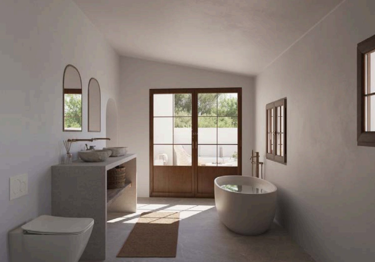 Salle de bains de luxe avec baignoire îlot, vasques en pierre et portes en bois ouvrant sur une terrasse ensoleillée.