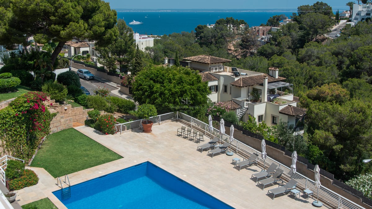 Vue aérienne d'une piscine bleue et terrasse avec chaises longues surplombant la Méditerranée et les villas.