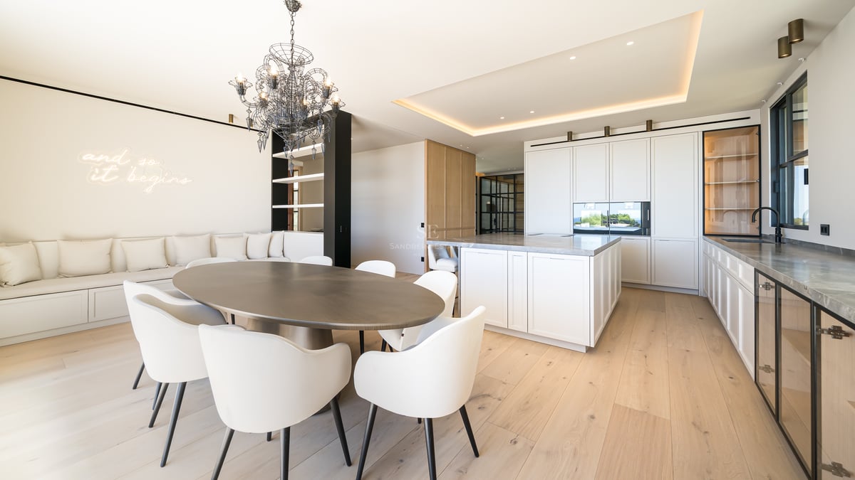 Une salle à manger spacieuse et moderne avec table ovale en bois, chaises blanches et cuisine intégrée.
