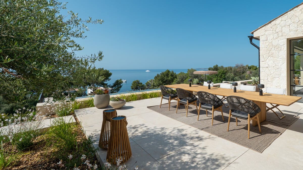 Grande table à manger en bois sur une terrasse en pierre naturelle offrant une vue panoramique sur la mer.