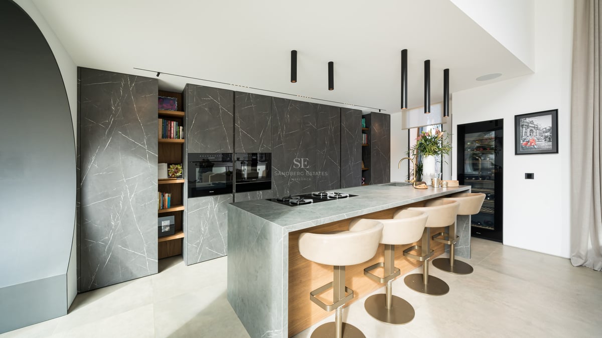 Cuisine moderne, placards marbre anthracite, îlot en pierre grise avec bar et suspensions design noires.