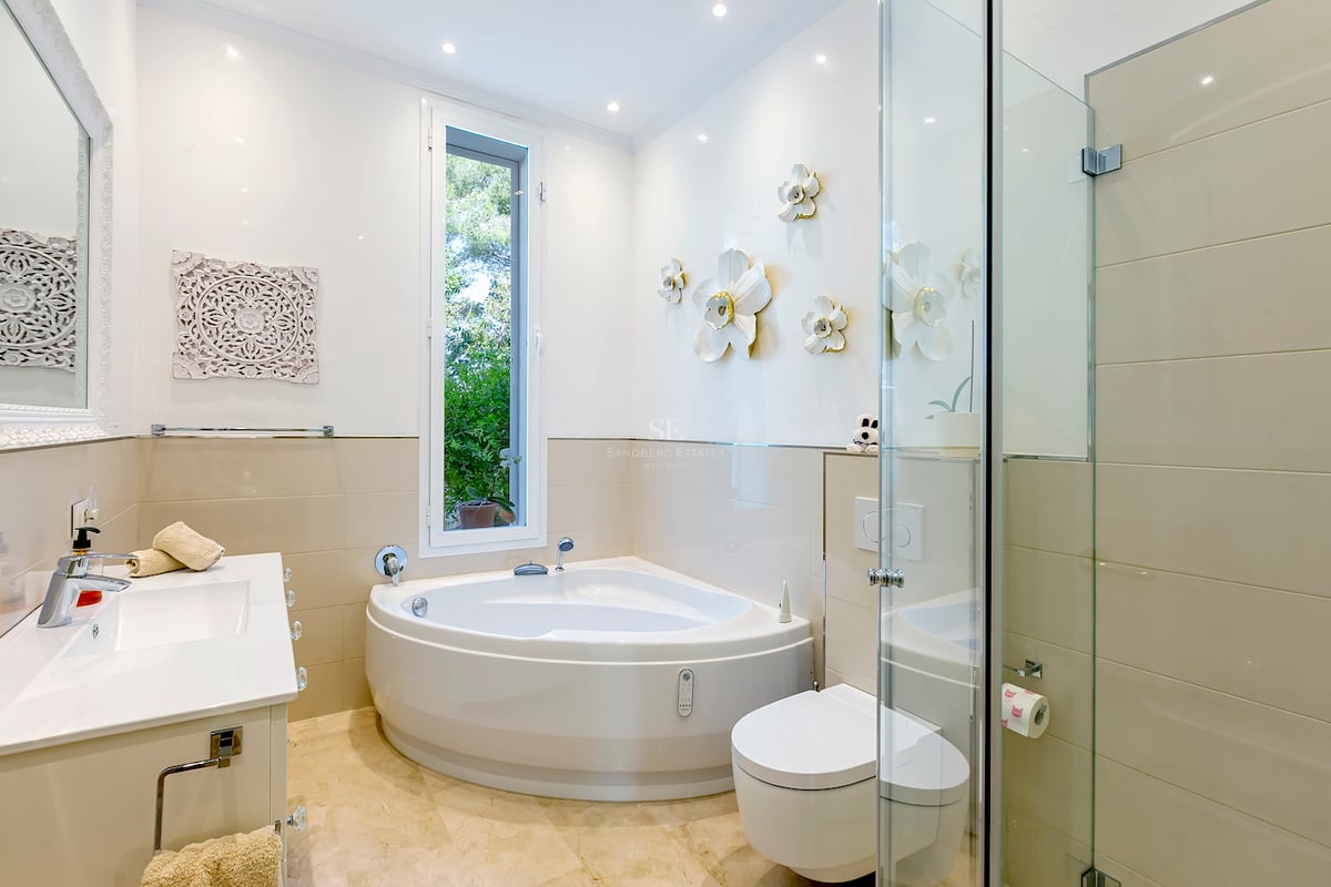 Salle de bains lumineuse avec baignoire balnéo, douche en verre, sol en marbre et vue sur le jardin.