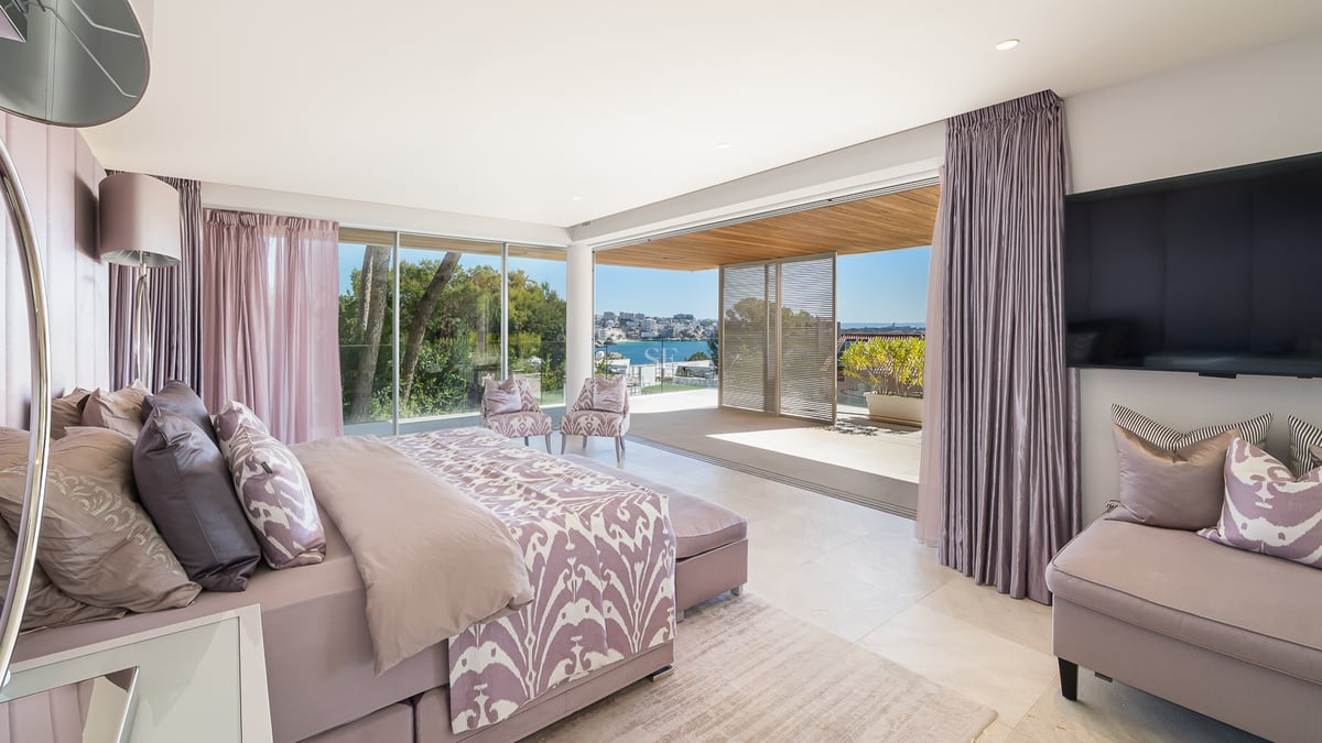 Chambre de maître lumineuse avec lit double, deux fauteuils et terrasse privée offrant une vue sur la mer.