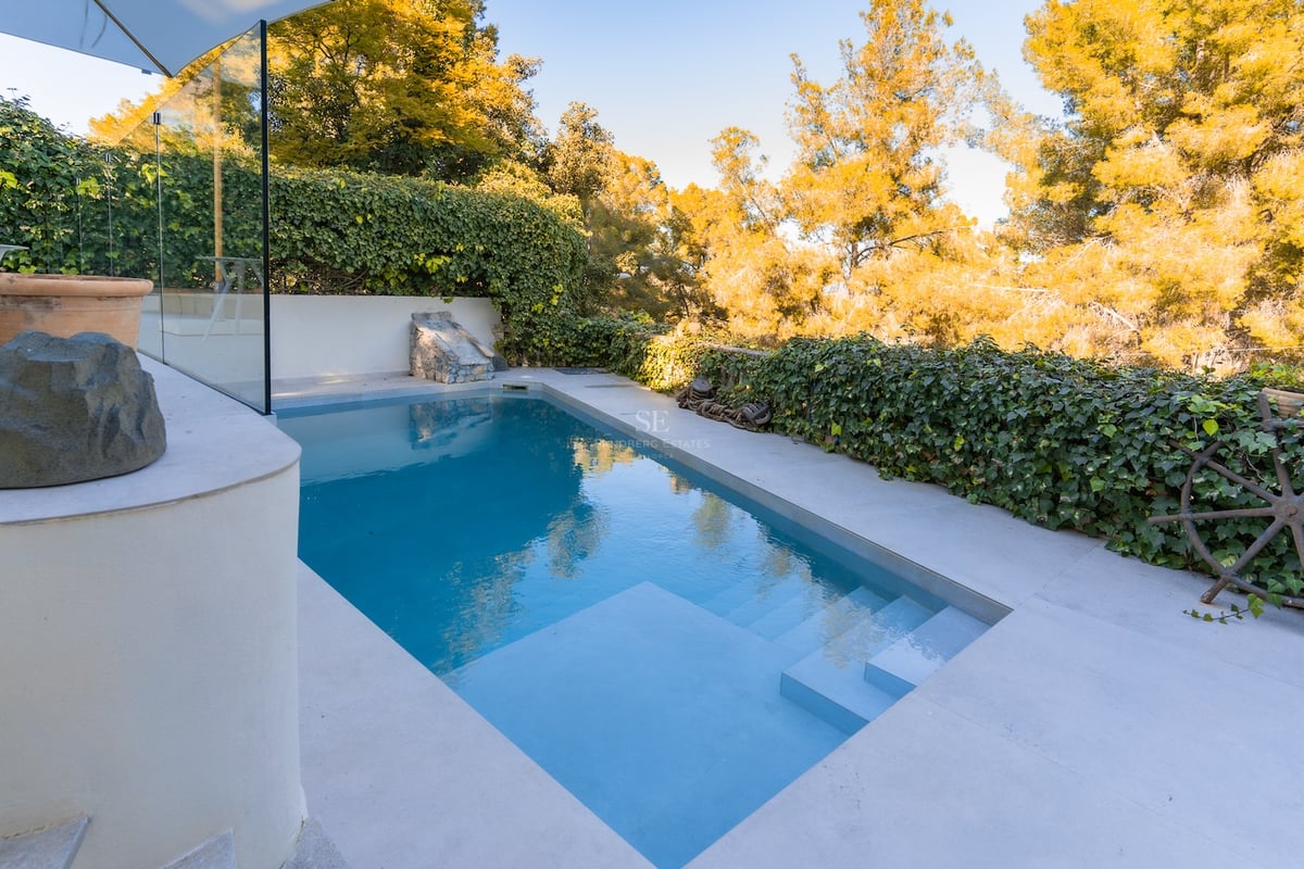 Piscine turquoise avec marches intégrées, entourée de dalles en pierre claire et de murs de lierre.