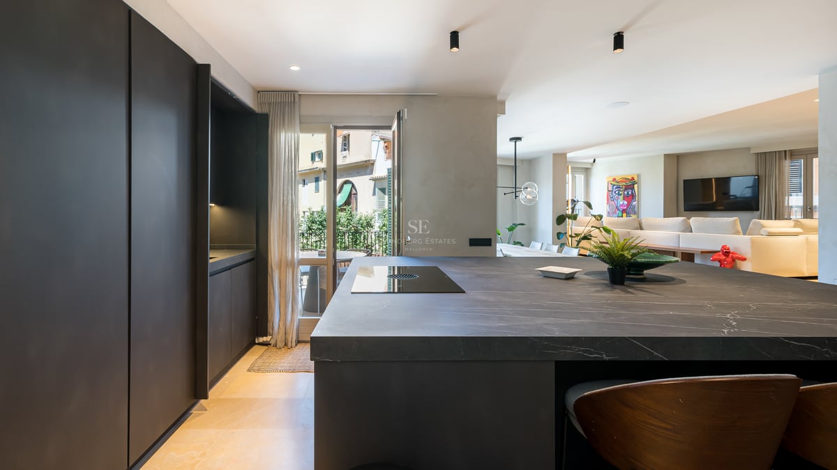 Cuisine contemporaine dotée d'un grand îlot en pierre noire, de rangements sombres et d'un sol en pierre claire.