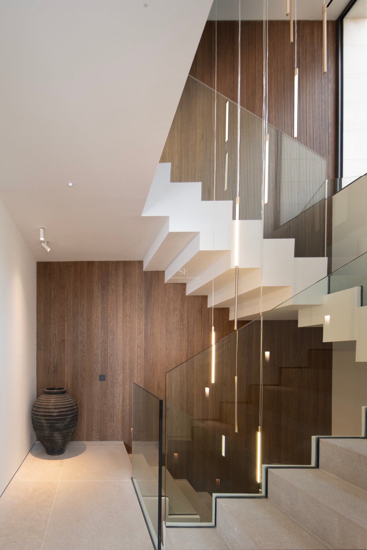 Escalier intérieur contemporain avec marches blanches, garde-corps en verre et panneaux muraux en bois vertical.