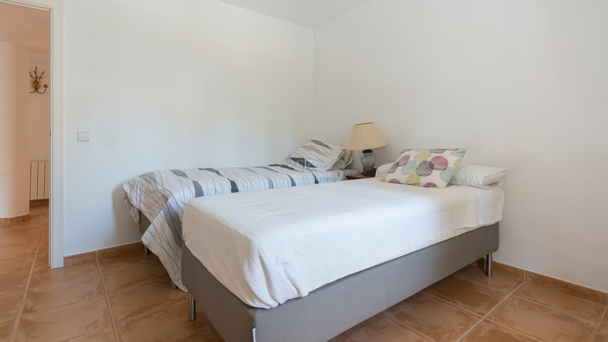 Chambre sobre avec deux lits simples, sol en terre cuite et murs blancs.