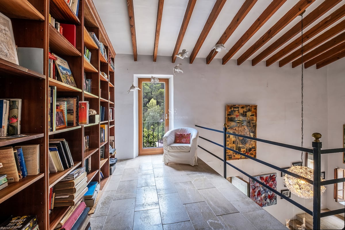 Bibliothèque en mezzanine avec étagères en bois du sol au plafond, sol en pierre et poutres apparentes.