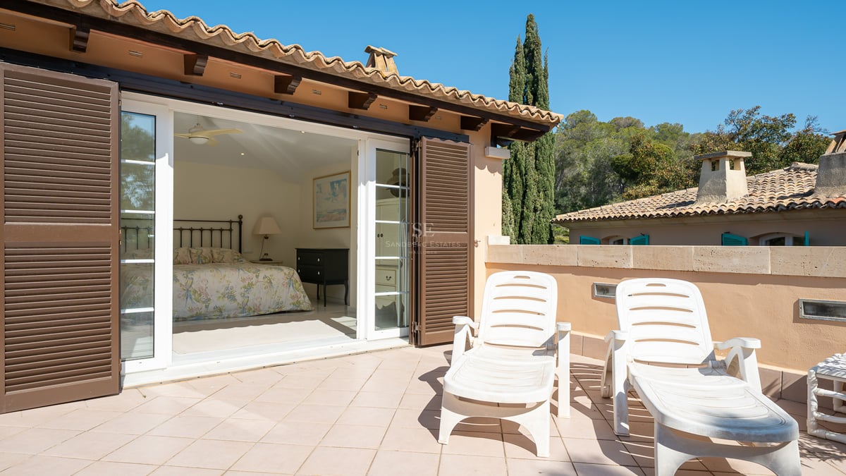 Chambre avec lit en fer forgé s'ouvrant sur une grande terrasse en terre cuite avec deux chaises longues.