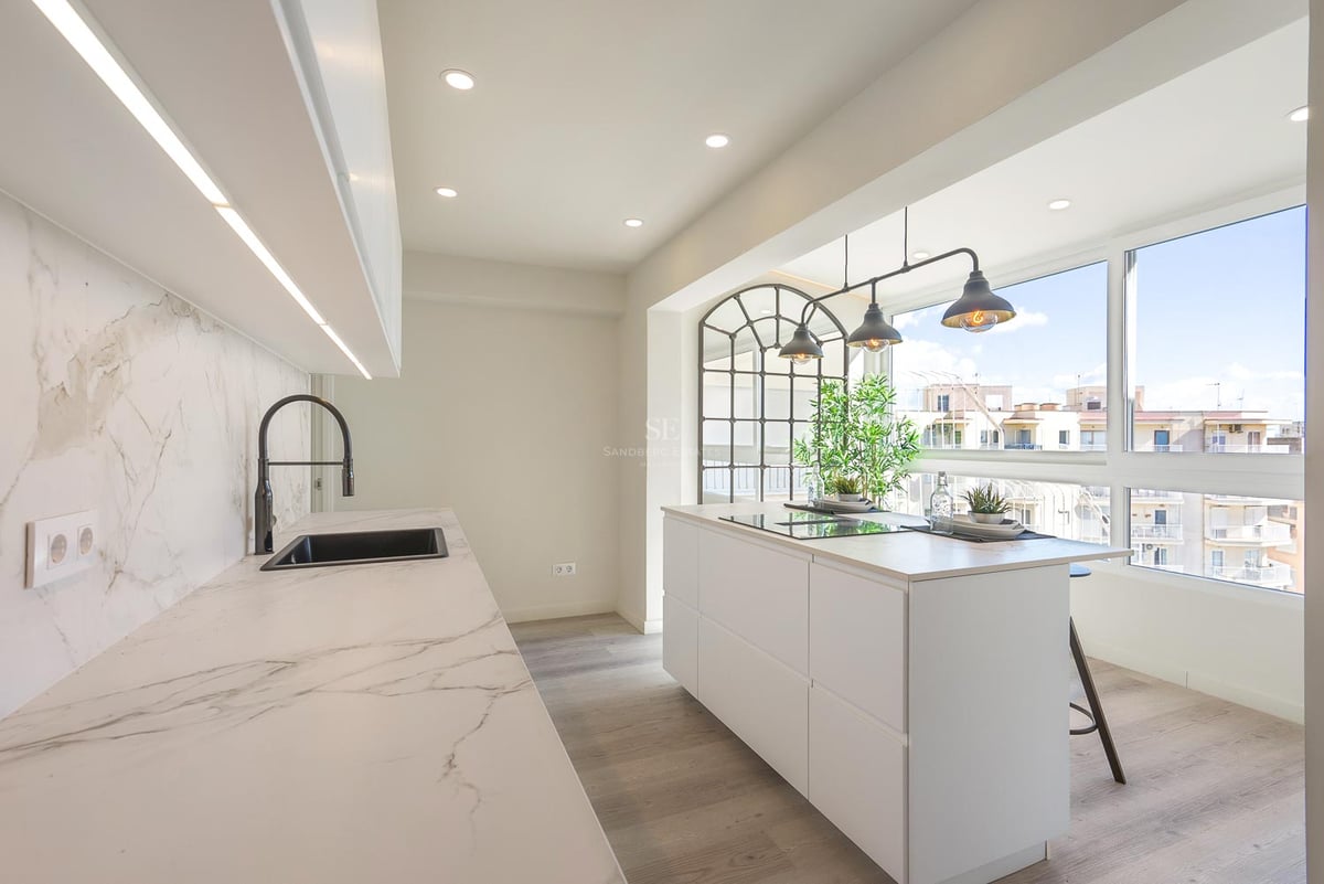 Cuisine blanche contemporaine avec îlot en marbre, suspensions industrielles et grandes fenêtres vue ville.