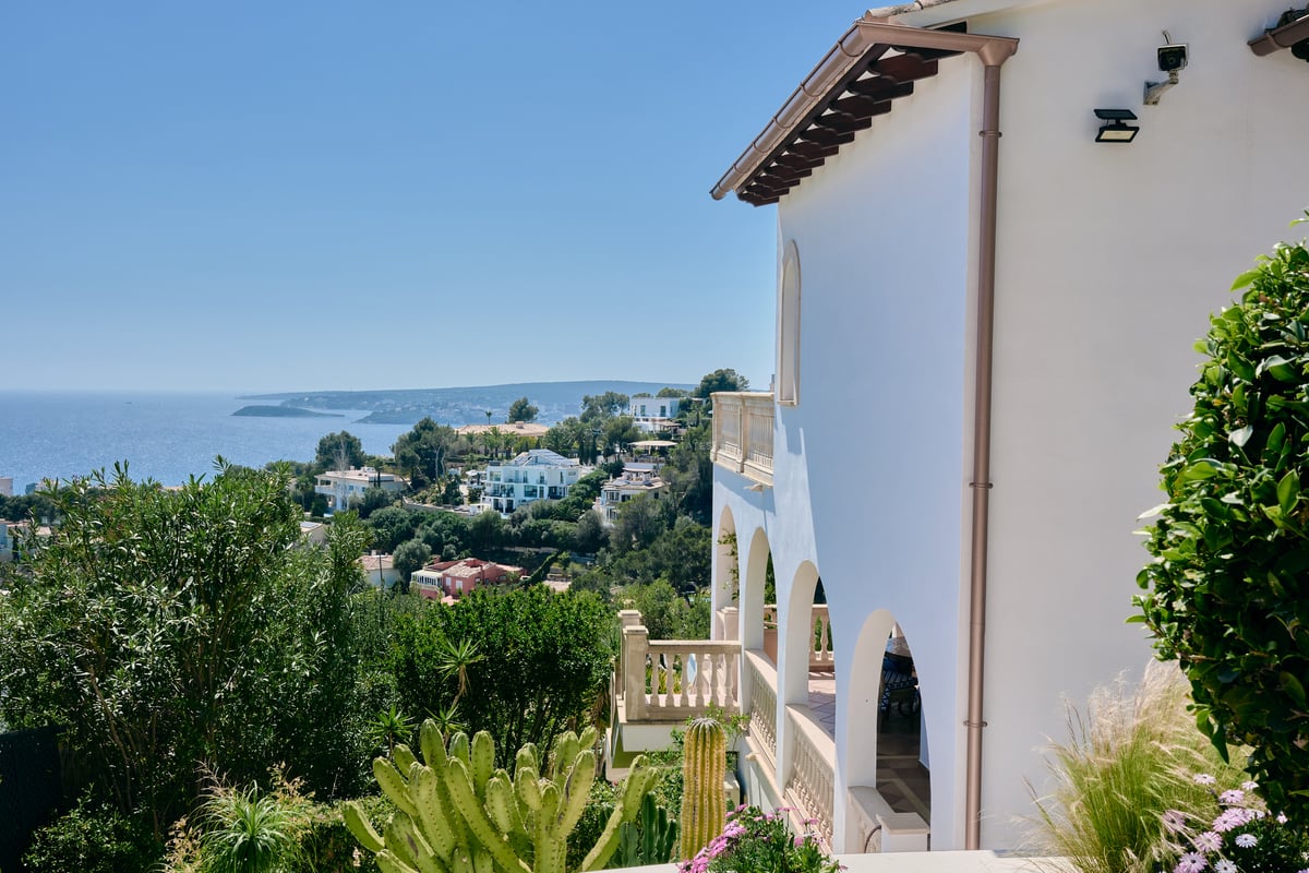 Vue latérale d'une villa blanche avec terrasses à arcades surplombant la côte et la mer Méditerranée.