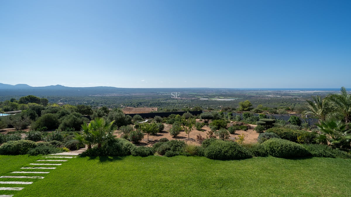 Vue de piscine à débordement avec transats et jardin luxuriant. Architecture moderne avec larges baies vitrées et ciel dégagé.
