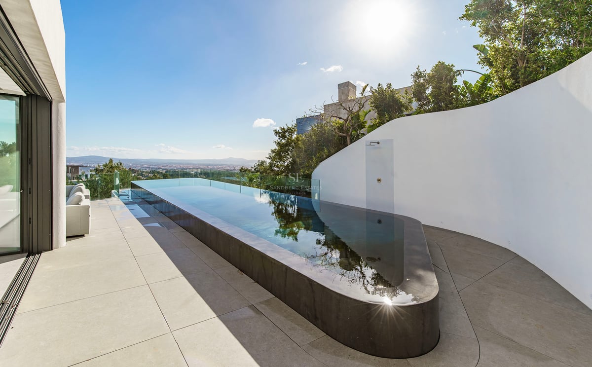 Une piscine à débordement élégante sur une terrasse blanche minimaliste surplombant la ville sous un ciel bleu.