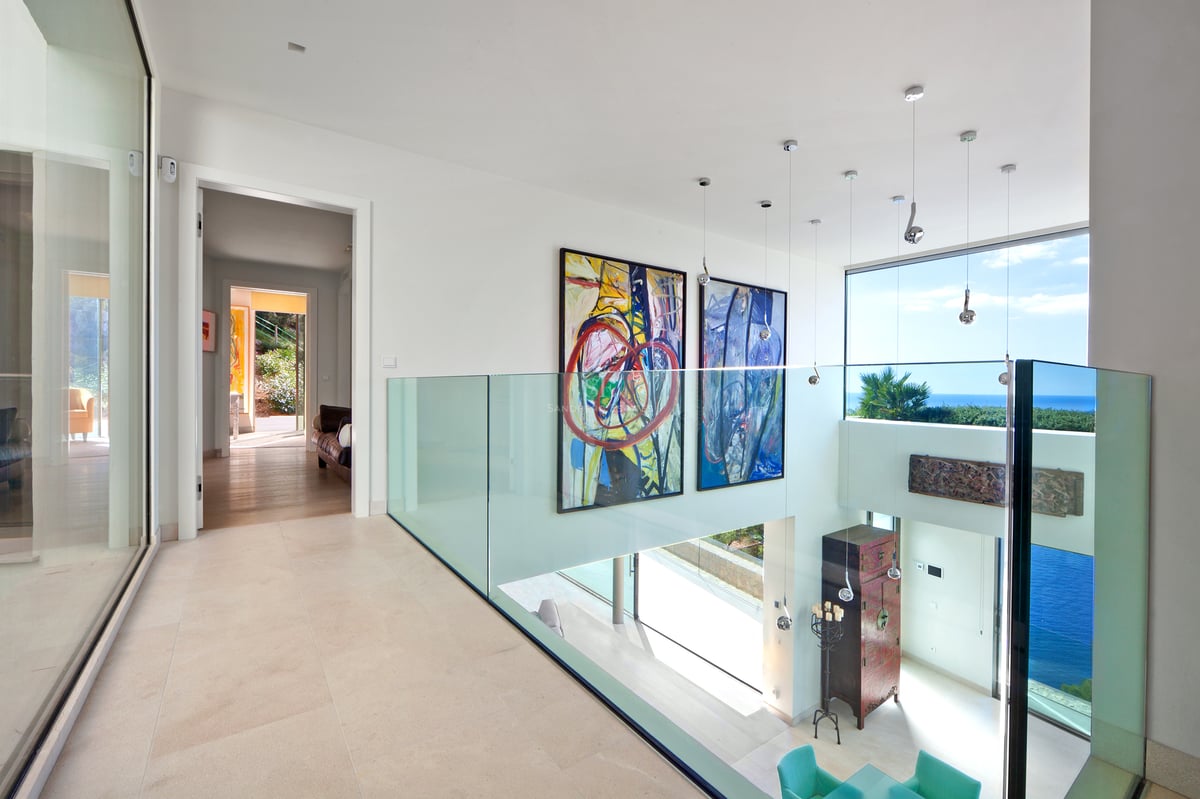 Couloir moderne avec garde-corps en verre, grands tableaux et vue sur la mer à travers de larges fenêtres.