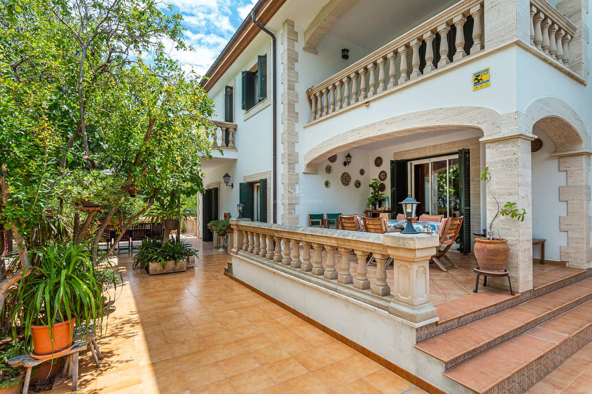 Terrasse en terre cuite avec balustrades en pierre, table à manger ombragée et arbres verdoyants.