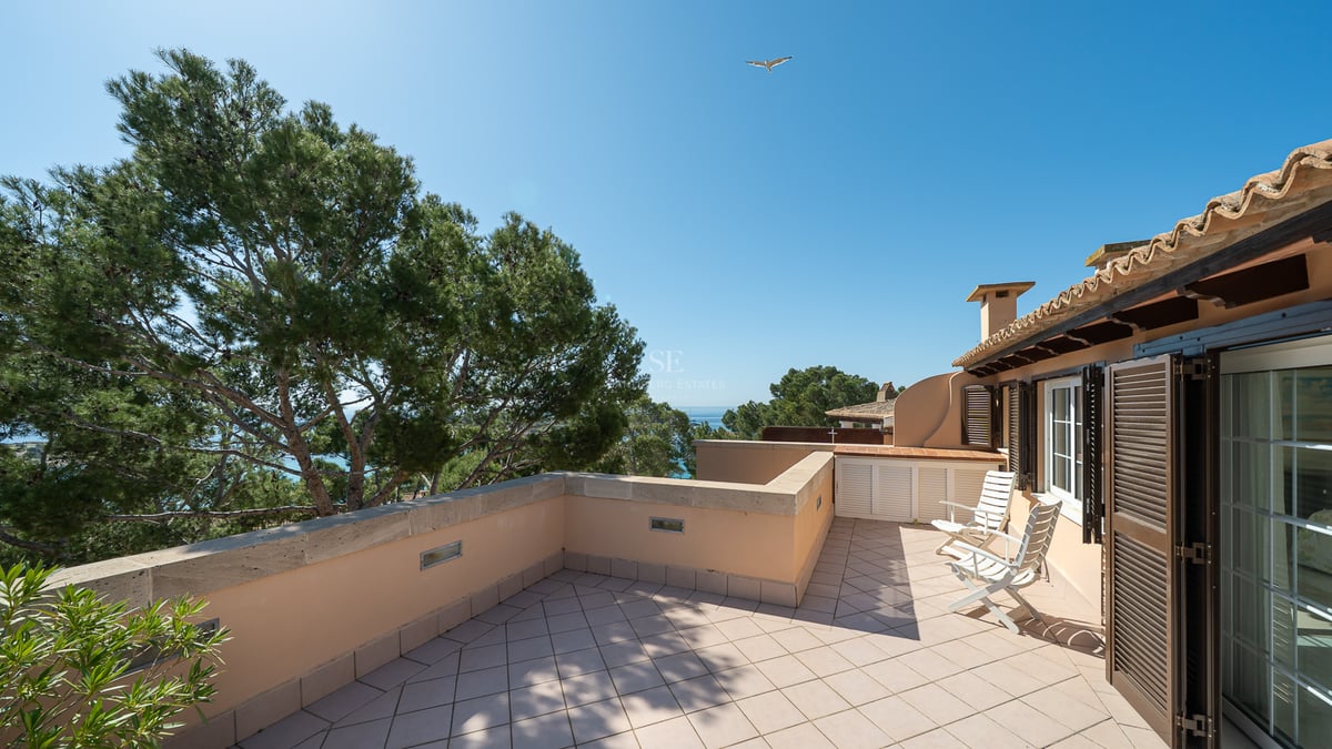 Terrasse ensoleillée avec carrelage en terre cuite, chaises blanches et volets traditionnels surplombant les pins et la mer.