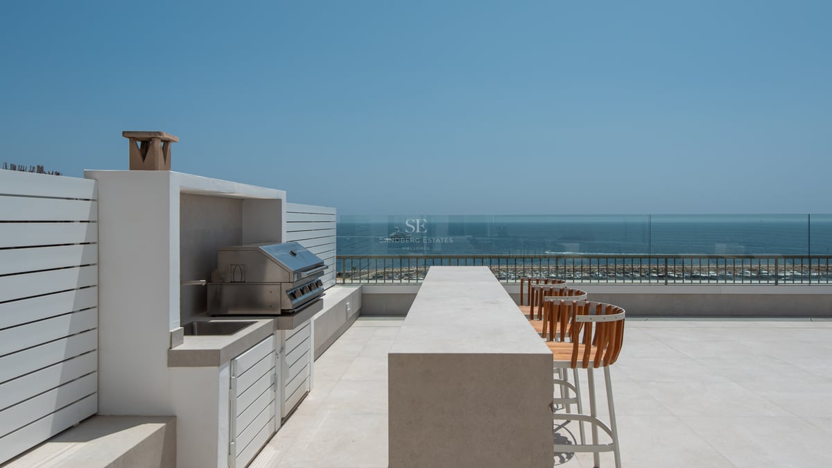 Terrasse moderne sur le toit avec cuisine d'été, bar en béton et tabourets en bois surplombant la mer et le port.