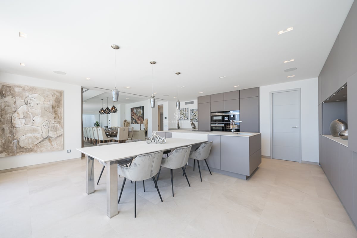 Cuisine moderne avec placards gris, îlot blanc avec table à manger et chaises en velours gris.
