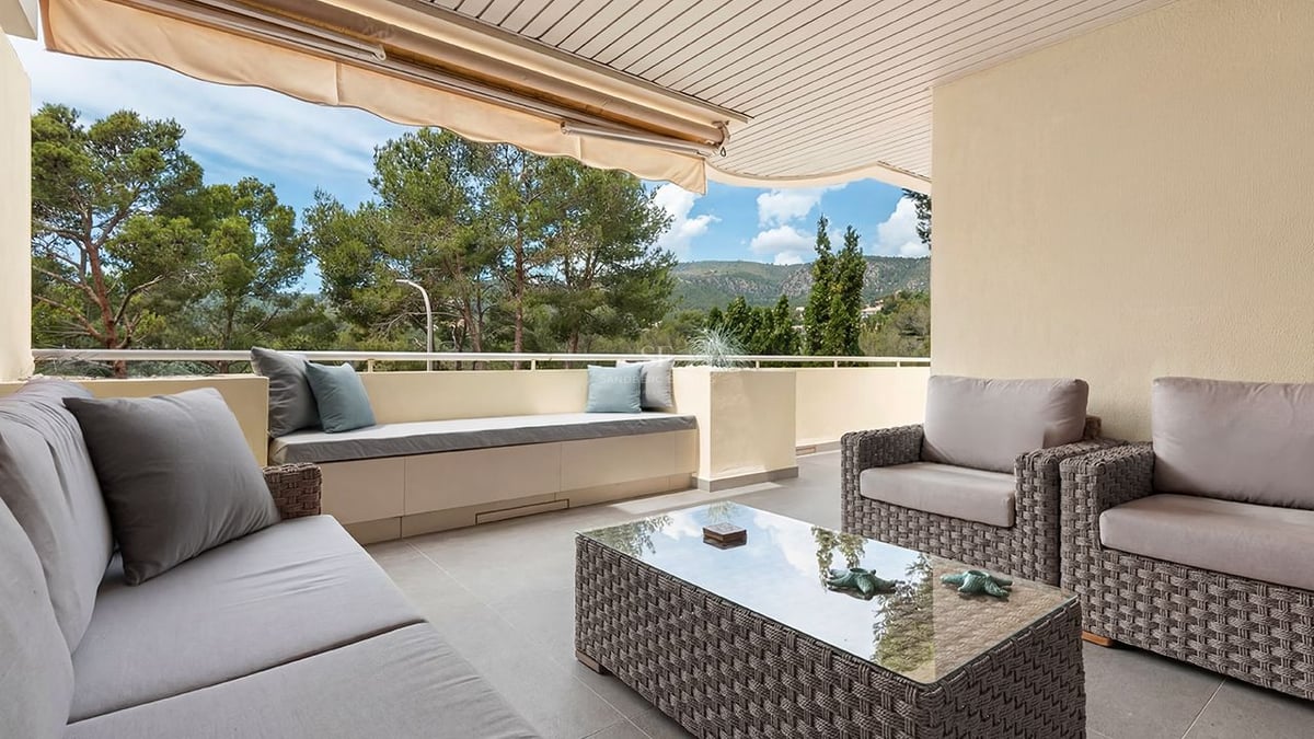 Terrasse couverte avec mobilier en osier gris, banc intégré et vue sur les pins et les montagnes.