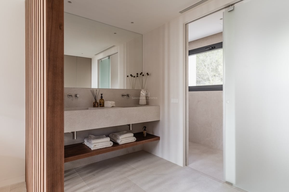 Salle de bain moderne dotée d'une double vasque en pierre beige, d'un mur en tasseaux de bois et d'une porte dépolie.
