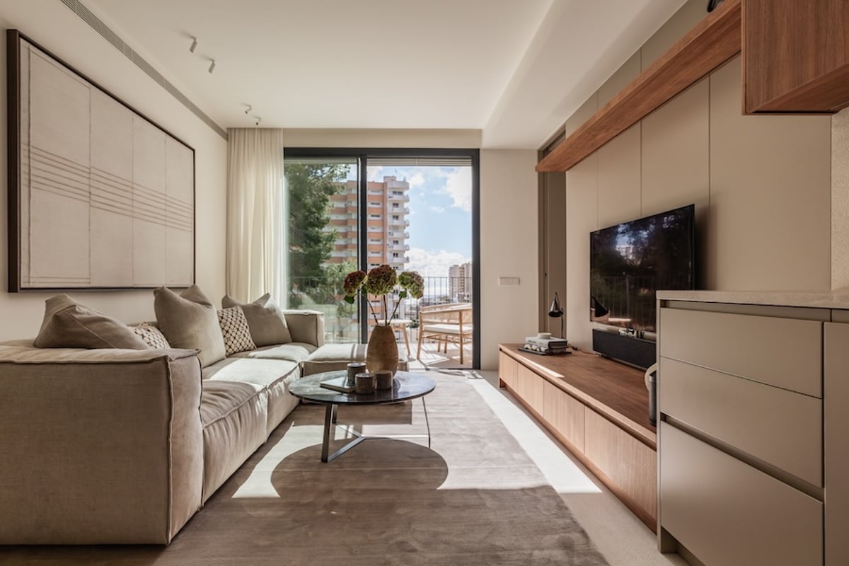 Salon lumineux avec un grand canapé beige, une table basse en marbre et des baies vitrées ouvrant sur un balcon.