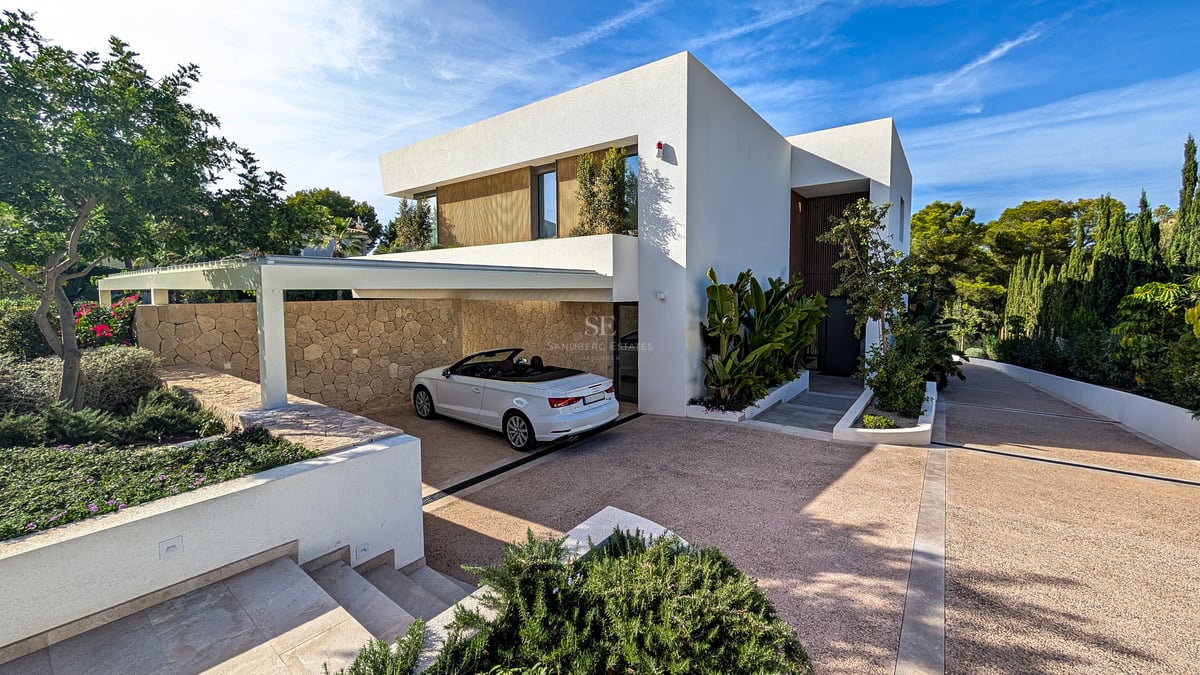 Villa blanche moderne avec une décapotable garée dans un abri aux murs de pierre naturelle sous un ciel bleu.