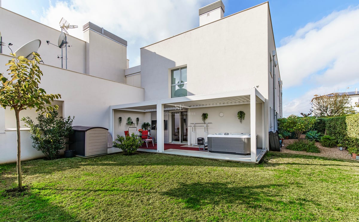 Un bâtiment blanc moderne avec une pelouse verte et une terrasse couverte comprenant un jacuzzi et un coin repas.