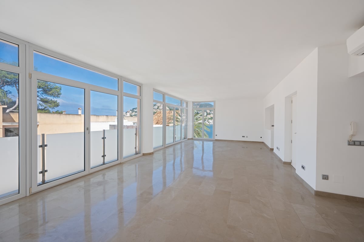 Salon moderne vide avec sol en marbre poli et grandes baies vitrées donnant sur la côte méditerranéenne.