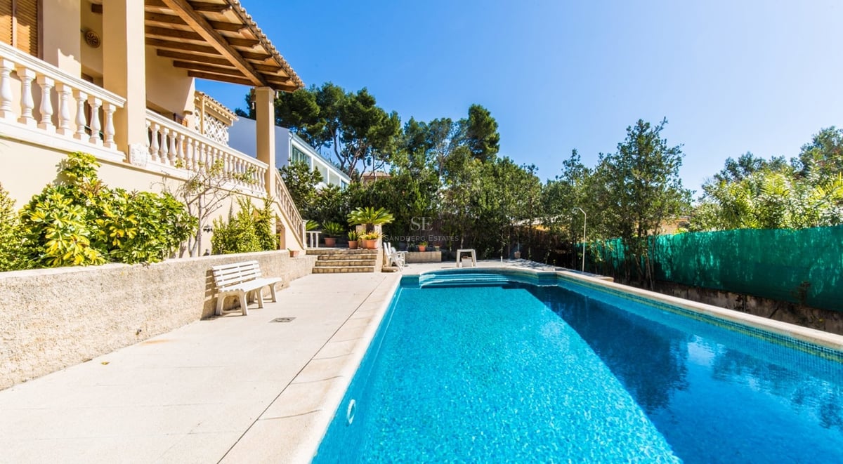 Une grande piscine rectangulaire bleue à côté d'une villa de style méditerranéen avec terrasse en pierre et verdure.