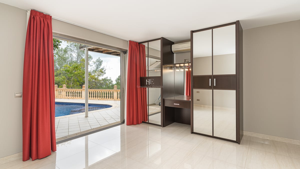 Chambre moderne avec rideaux rouges, armoires à miroirs et coiffeuse, donnant sur une piscine via des baies vitrées.