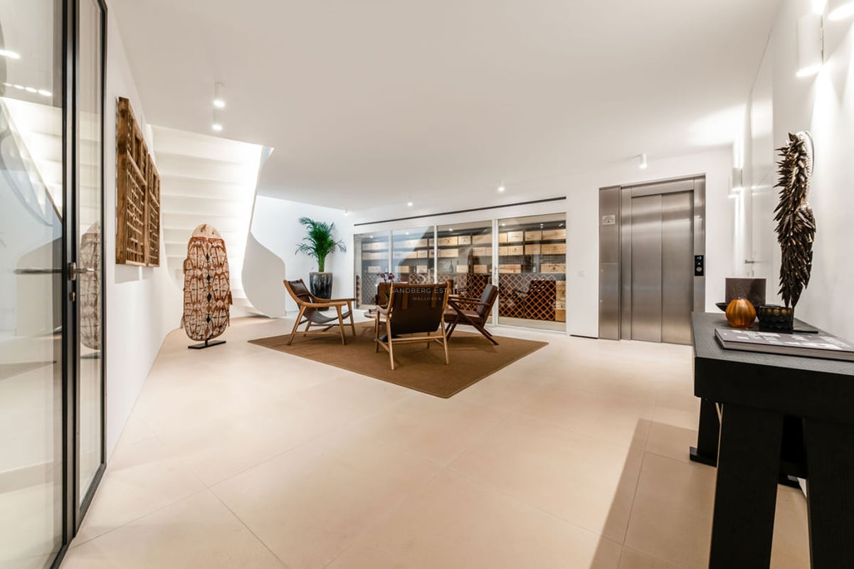Hall minimaliste avec cave à vin vitrée, ascenseur en acier inoxydable, escalier en colimaçon blanc et fauteuils en cuir.
