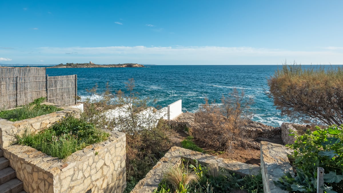 Terrasse en pierre naturelle surplombant une mer d'un bleu profond avec une petite île à l'horizon sous un ciel clair.
