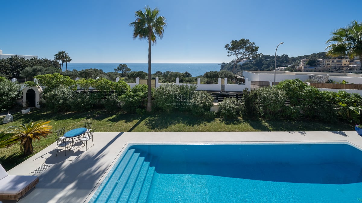 Piscine bleue entourée d'un jardin avec vue directe sur la Méditerranée sous un ciel clair.