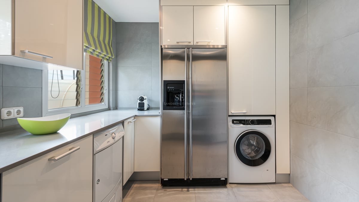Espace buanderie avec réfrigérateur américain en inox, lave-linge et placards blancs sur carrelage gris.